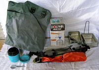 Camping essentials include a green waterproof bag, Dolphin water pump in box, blue thermos with lid and spoon, two aluminum dishes with utensils, and two belts (black and orange).