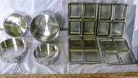 Wide view of four aluminum pans and four compartment trays with ruler underneath for size reference.
