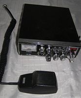 Galaxy DX 919 CB radio with microphone on table, showing front and side angle of the black metal box and attached coiled microphone cord.