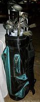 Full view of golf clubs inserted in the green and black shoulder golf bag, showing club heads and part of the bag's pocket.