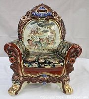 Front view of the ceramic chair sculpture showing detailed floral upholstery pattern and central landscape scene on backrest.