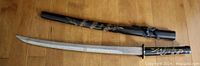 Full view of katana sword and its black lacquered wood scabbard with dragon decorations placed side by side.