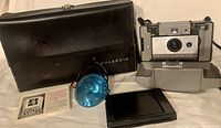 Polaroid Automatic 103 Land Camera with black carrying case, blue flash reflector, film holder, and instruction booklet laid out on surface.