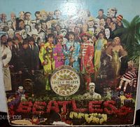 Front cover of Sgt. Pepper's Lonely Hearts Club Band album showing colorful collage artwork with The Beatles in military band outfits and surrounding figures, with 'BEATLES' spelled out in flowers at the bottom.
