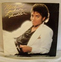Cover of Michael Jackson Thriller album showing Michael Jackson reclining in white suit and black shirt, with title text in gold.