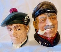 Pair of vintage Bossons chalkware sculptures showing front and side views against white background. One bust with green Scottish tam o'shanter hat with red pom-pom and white decoration, the other with captain's hat and a pipe.