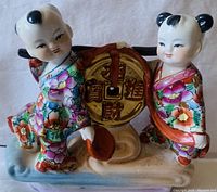 Front view of the colorful Chinese ceramic figurine showing two children holding a large golden coin with Chinese characters.