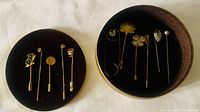 Photo showing 5 pins arranged on a black velvet cushion inside a circular box lid and 6 pins arranged inside the box to display variety