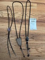 Three leather bolo ties laid out side by side showing varying clasp designs and braided leather cords.