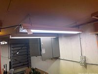White rectangular fluorescent hanging light fixture suspended from ceiling with two fluorescent tubes visible inside housing.