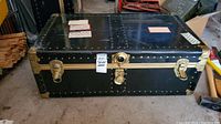 View of one Atlas Luggage Co. black travel trunk with metal corners, central lock, and two latches.