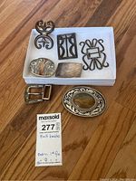 Overview of seven belt buckles in white tray and on floor