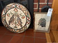 Photo showing two bird art pieces: large round ceramic tile mosaic and smaller framed linen painting.