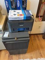 Brother HL-L2360DW printer on top of the file cabinet with cartridges and paper on top