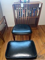 Front view of wooden chair with black upholstered seat and matching foot stool in front.
