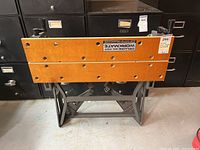 Front view of the Deluxe Dual Height Workmate showing wooden clamping surfaces with holes and metal folding legs.