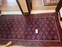 Full view of the large rectangular red and blue area rug lying on a wooden floor, showing its tassel fringe and geometric pattern.