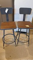 Pair of gray metal stools with wooden seats and backrests, showing overall weathered condition and structure details