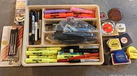 Top view of beige plastic organizer tray filled with highlighters, Sharpie markers, pens, and multiple tape measures