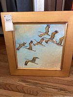 Full view of the framed painting showing multiple ducks flying against a blue sky.
