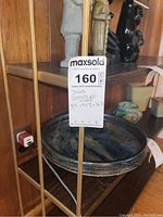 Close-up photo of shelving unit frame and shelf surface with sale tag showing measurements and details. A large dark blue bowl and decorative statues are visible but not included.