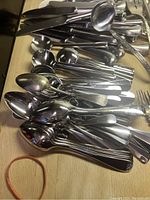 Large assortment of silverware laid out on wooden surface including spoons, forks, and knives of different styles and sizes.