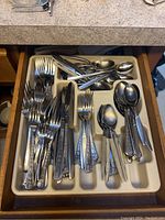 Drawer organizer containing multiple stainless steel forks, spoons and knives with decorative handles.