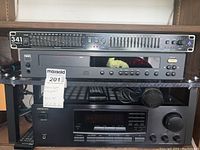 Stereo system gear on a wooden shelf: ART Dual 15 Band EQ 341 amplifier on top, NAD CD player 5000 in the middle, Onkyo stereo receiver at bottom with microphone and cables.