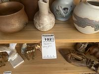 Wooden shelf with a collection of seven stoneware and pottery pieces including vases and pitchers in earth tones and various finishes.