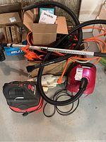 Full view of Craftsman wet/dry vacuum in black and red, Simplicity handheld vacuum in pink, metal wand, hoses, and assorted cords piled around them.