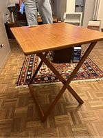Single wooden TV tray table set up on parquet floor with part of a patterned rug and office background visible.
