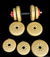 Loaded adjustable dumbbell assembled with several vinyl-coated gold weight plates and red collars securing weights on the black textured handle bar
