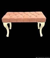 Front view of pink tufted upholstered bench with white curved plastic legs.