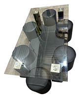 Top view of glass table with uniquely shaped inner glass inset and six black side stools arranged around it.