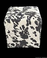 Front view of cube ottoman with black and white cow print suede fabric.