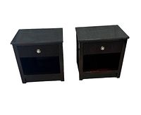 Front view of the two black side tables showing marble tops, single drawers with silver knobs, and open shelves below