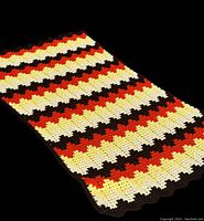 Full view of the flat crocheted afghan showing the zig zag color pattern in fall tones on a black background.