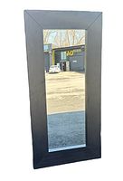 Front view of large rectangular wall mirror with black wooden frame reflecting outdoor scene, showing clear mirror surface and wide frame.