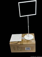 Six large white adjustable sign holders, one displayed on top of a cardboard box showing metal base and rectangular frame.