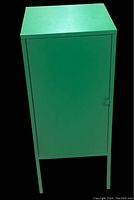 Front view of the green metal cabinet showing the door with round handle and four legs.