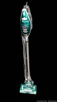 Front view of the full Shark Rocket DeluxePro vacuum cleaner showing its upright, slim design, green and silver color, handle with power switch, power cord wrapped around the tube, and motorized brush head with clear window.
