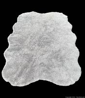 Full view of the natural rolled wool rug showing its organic shape and wool texture against a black background.