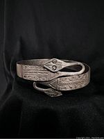 Front view of silver-colored metal bracelet featuring double snakehead design, showing stamped geometric patterns on the wide band.