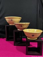 Three antique yellow ware bowls displayed on black stands, showing various sizes and slip dot decoration on yellow-beige glaze.