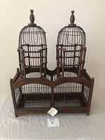 Front view of the double birdcage showing wood and wire construction and two cage sections with wooden doors and finials.