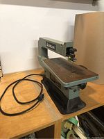 Front left view of Delta scroll saw showing the metal work table, saw arm with Delta branding, and attached power cord.