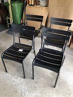 Four black stackable Fermob Luxembourg patio chairs in garage with two armchairs and two armless chairs visible, showing design and wear.