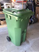 Green plastic rectangular bin with lid closed, showing side profile with wheels at back and handles.