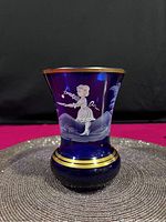 Front view of cobalt blue vase with white enamel Mary Gregory style figure and gold rim.