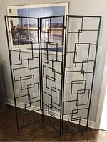 Front angled view showing three panels of the metal room divider with intricate geometric square shapes.